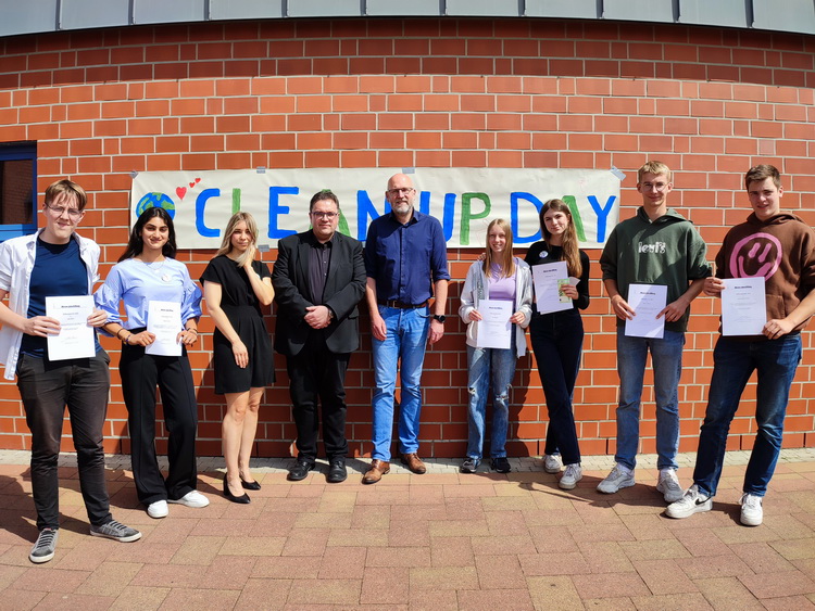 J. Gerlach, Schulleiter M. Zilk und K. Schwettmann (Mitte) zusammen mit für ihr soziales Engagement ausgezeichneten Schüler:innen auf dem "Clean Up-Day" 